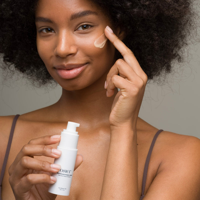 Model smiling as she applies Osier Vitamin C Serum, bottle in hand