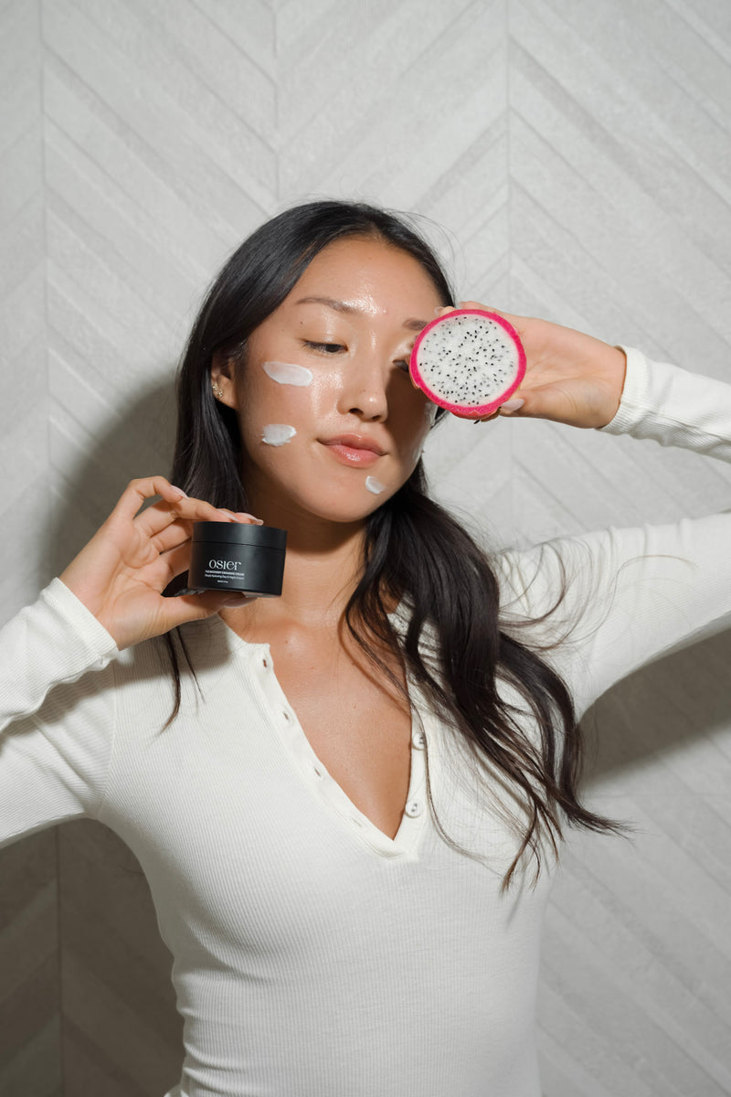 Model with cream on her face holding a dragon fruit and Osier Recovery Ceramide Cream